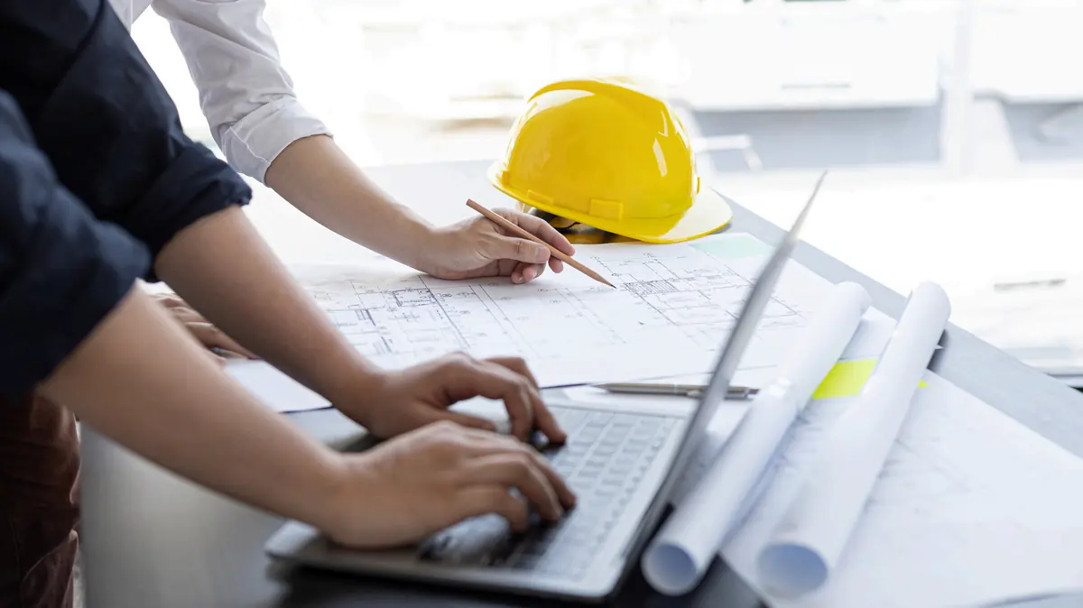 Deux ingénieurs travaillant sur des plans, un casque de chantier jaune posé sur la table